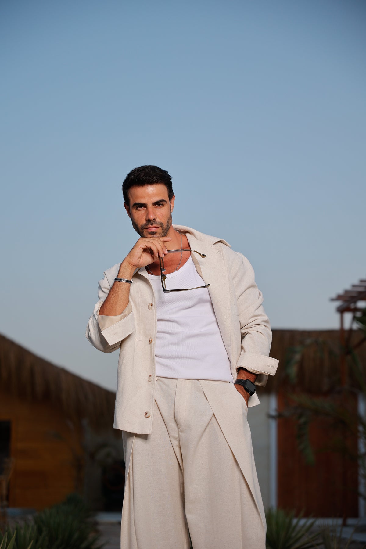 Man wearing the RAZ STUDIO RAZ-05 sand linen jacket with rolled sleeves, holding eyeglasses near his face